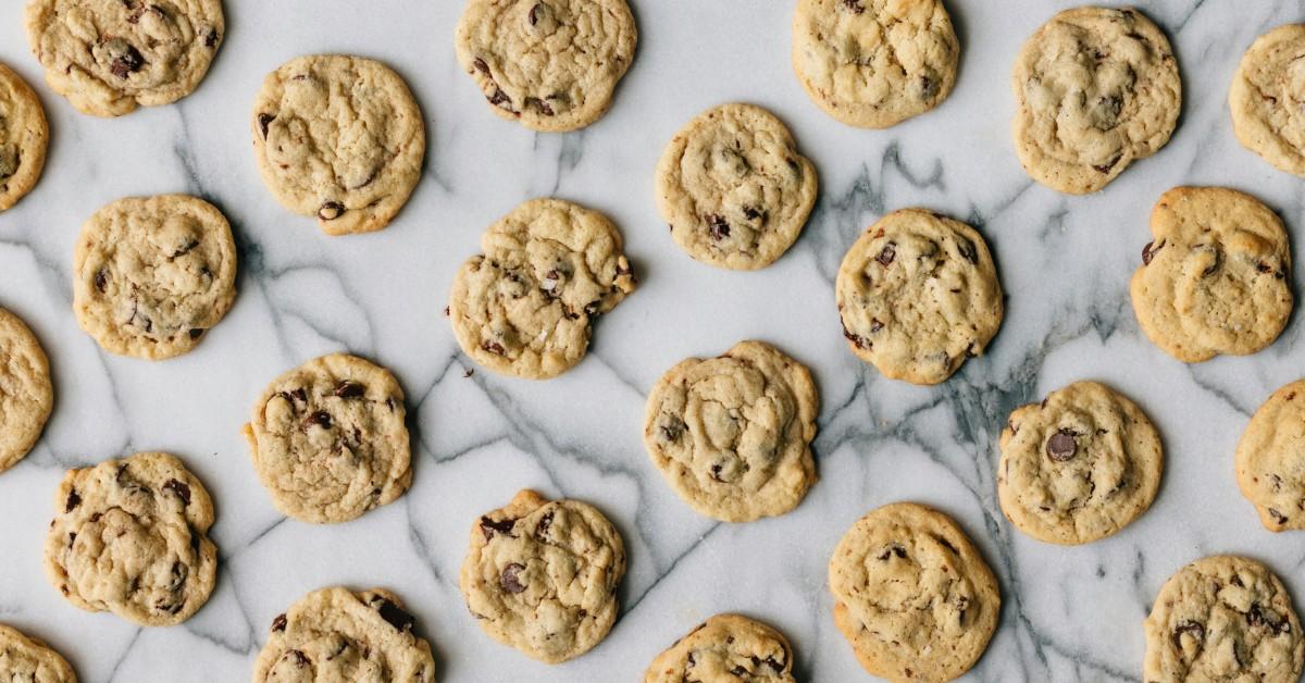 Rows of chocolate chip cookies sit out on a marble countertop 