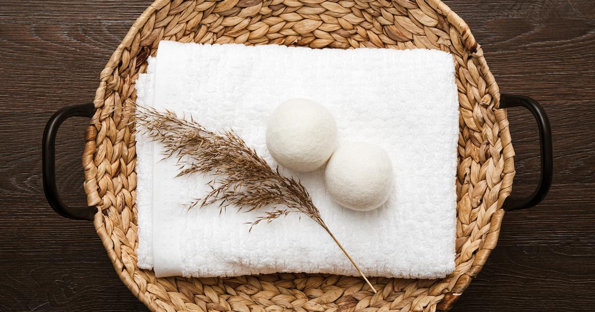 Two dryer balls sit on top of a folded white towel in a wicker laundry basket