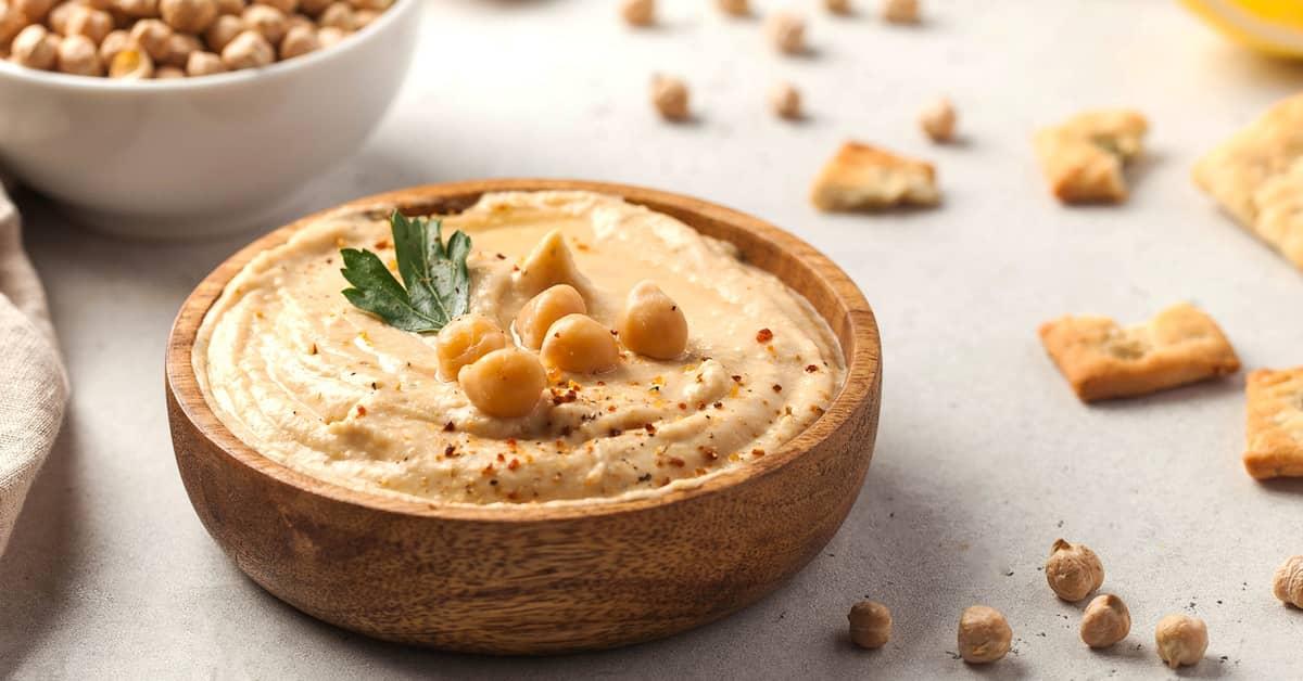 Wooden bowl filled with cream-looking hummus, garnished with chickpeas