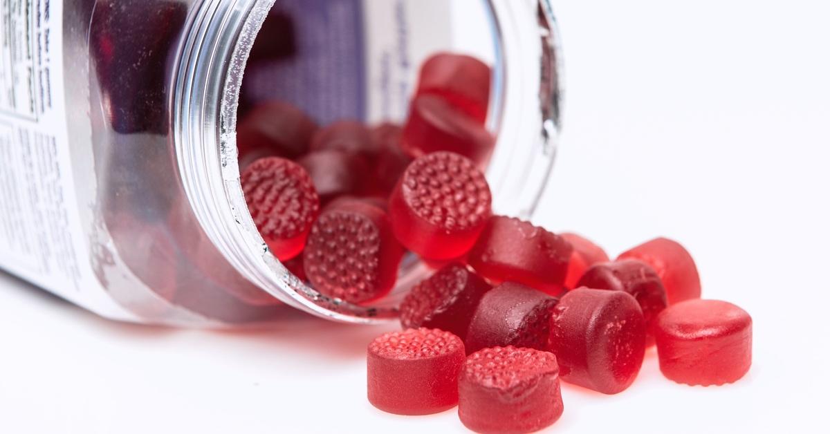 Red circular gummies spilling out of an open plastic container. 