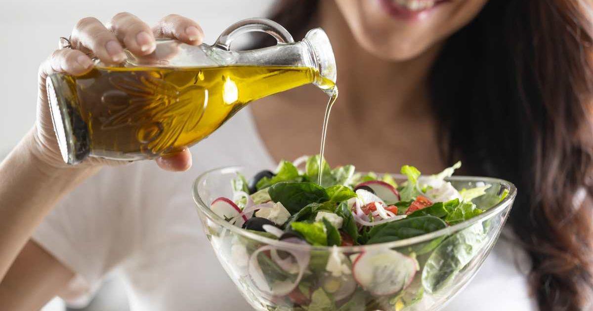 Woman pouring soyabean oil from a glass jar into a bowl of salad while smiling (Represesntative Cover Image Source: Getty Images | Simple Images)