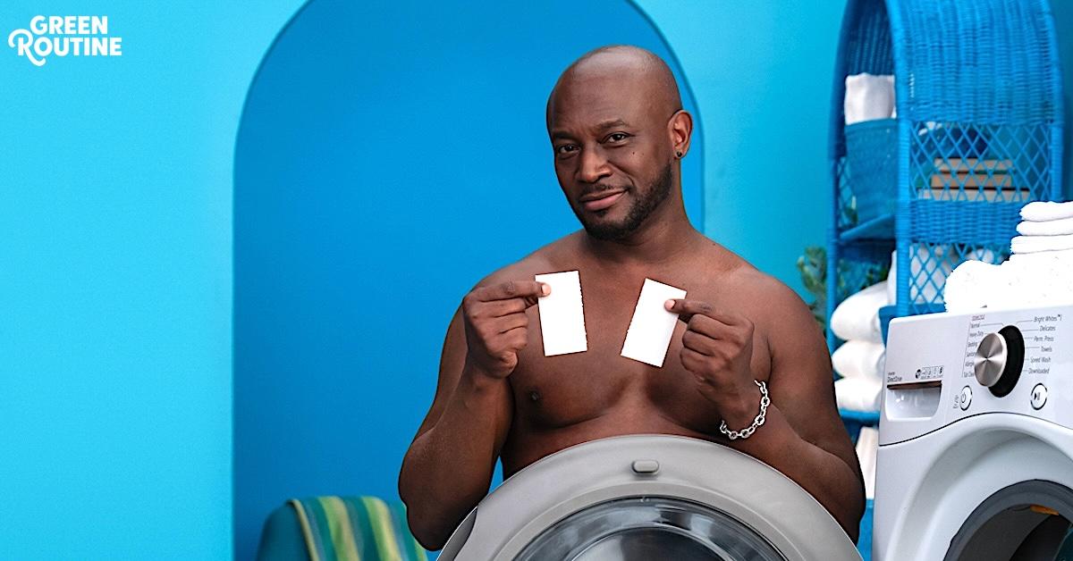 Closeup of Taye Diggs topless, as he smirks and stands nude with a washing machine blocking his body, and holds up Tru Earth's laundry eco-strips