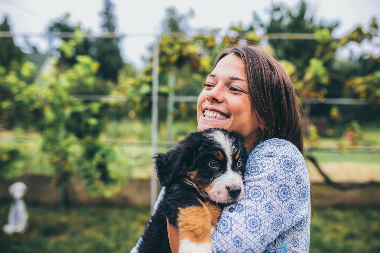 A smiling woman holds her puppy in an outdoor garden