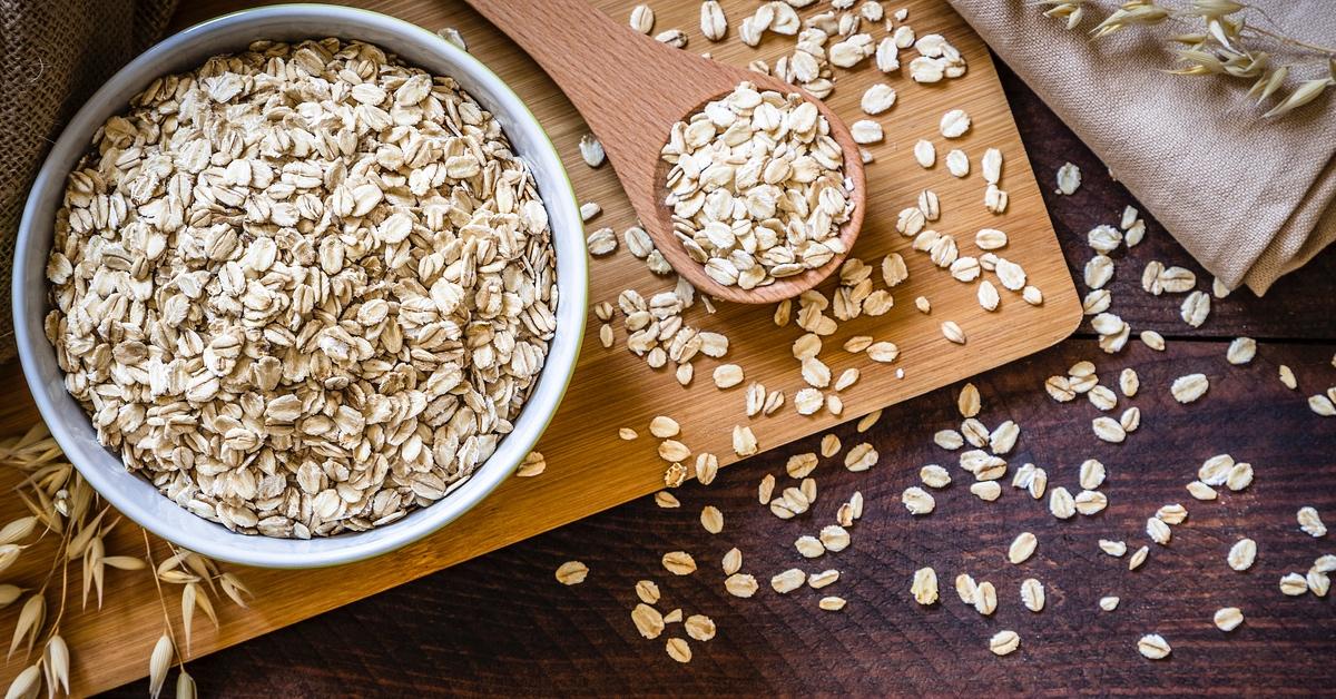 Bowl of oats and spoonful of oats on a wooden table.