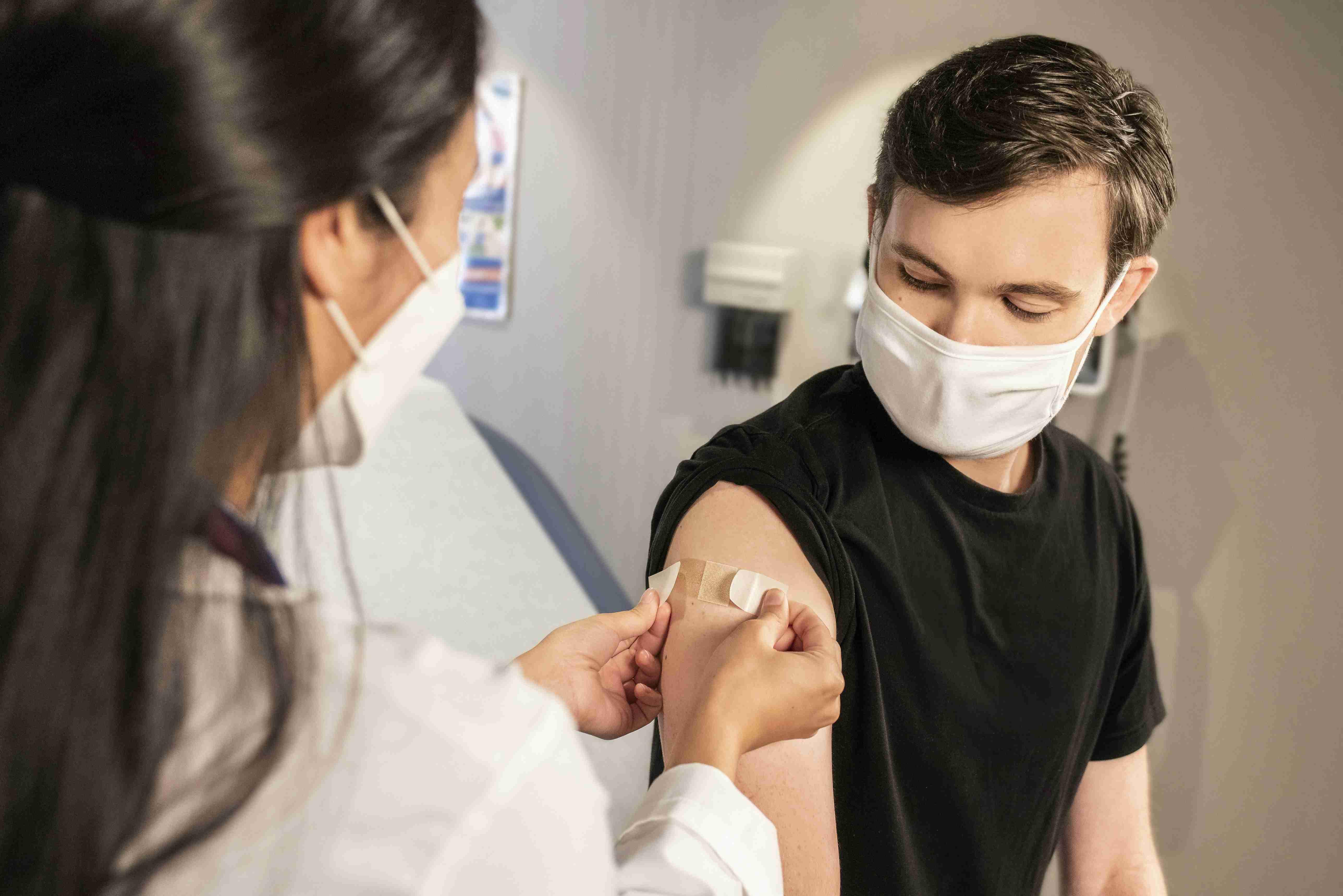 A masked doctor places a bandage over the right arm of a patient who is also wearing a mask.