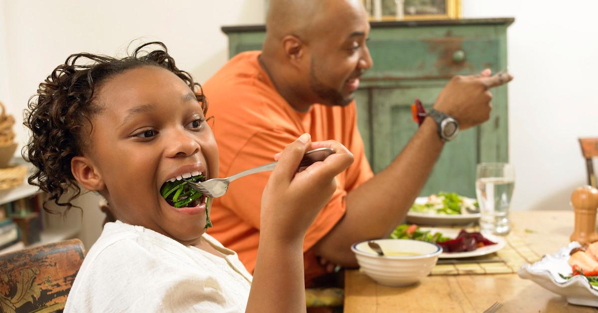 Two people sitting at Thanksgiving dinner, the girl in the front of the frame is putting vegetables into her mouth.