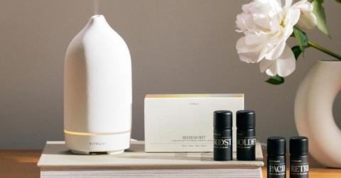 Photo of a Vitruvi oil diffuser sitting on a book beside small black bottles of various Vitruvi essential oils