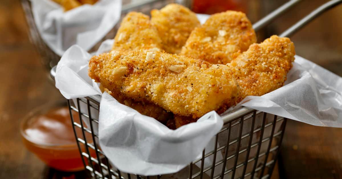 Basket of crispy vegan chicken nuggets with dipping sauce on the side.