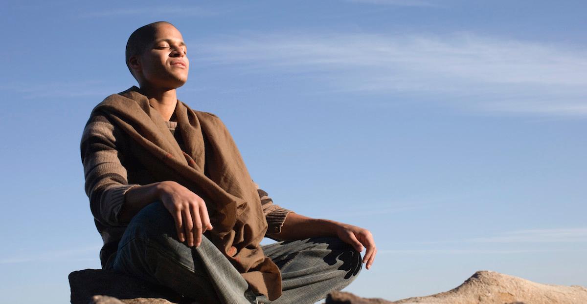 A person meditates on a rock outside.