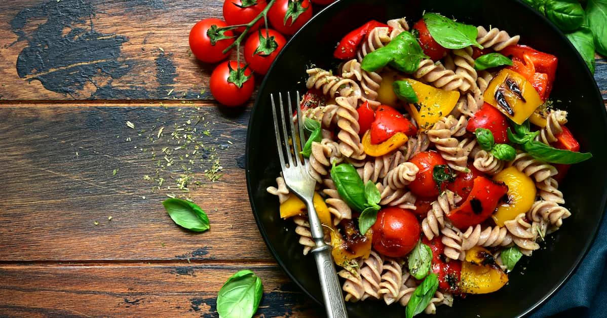 A delicious plate of pasta with tomatoes and red and yellow peppers, and garnished with fresh basil