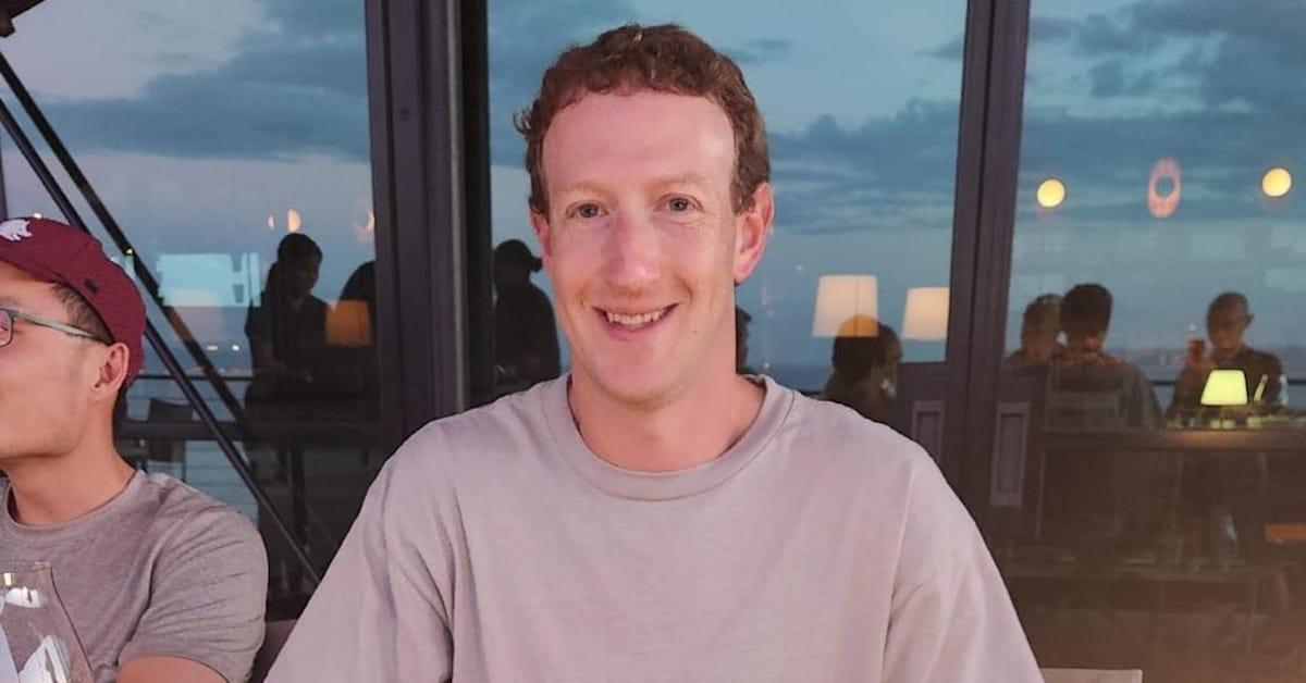 Mark Zuckerberg sits at a table with beef out of frame, with the sky seen in the reflection in the background