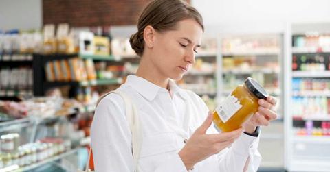 Woman looks at the label of a jar of honey at the grocery store. (Representative Cover Image Source: Freepik | freepik)