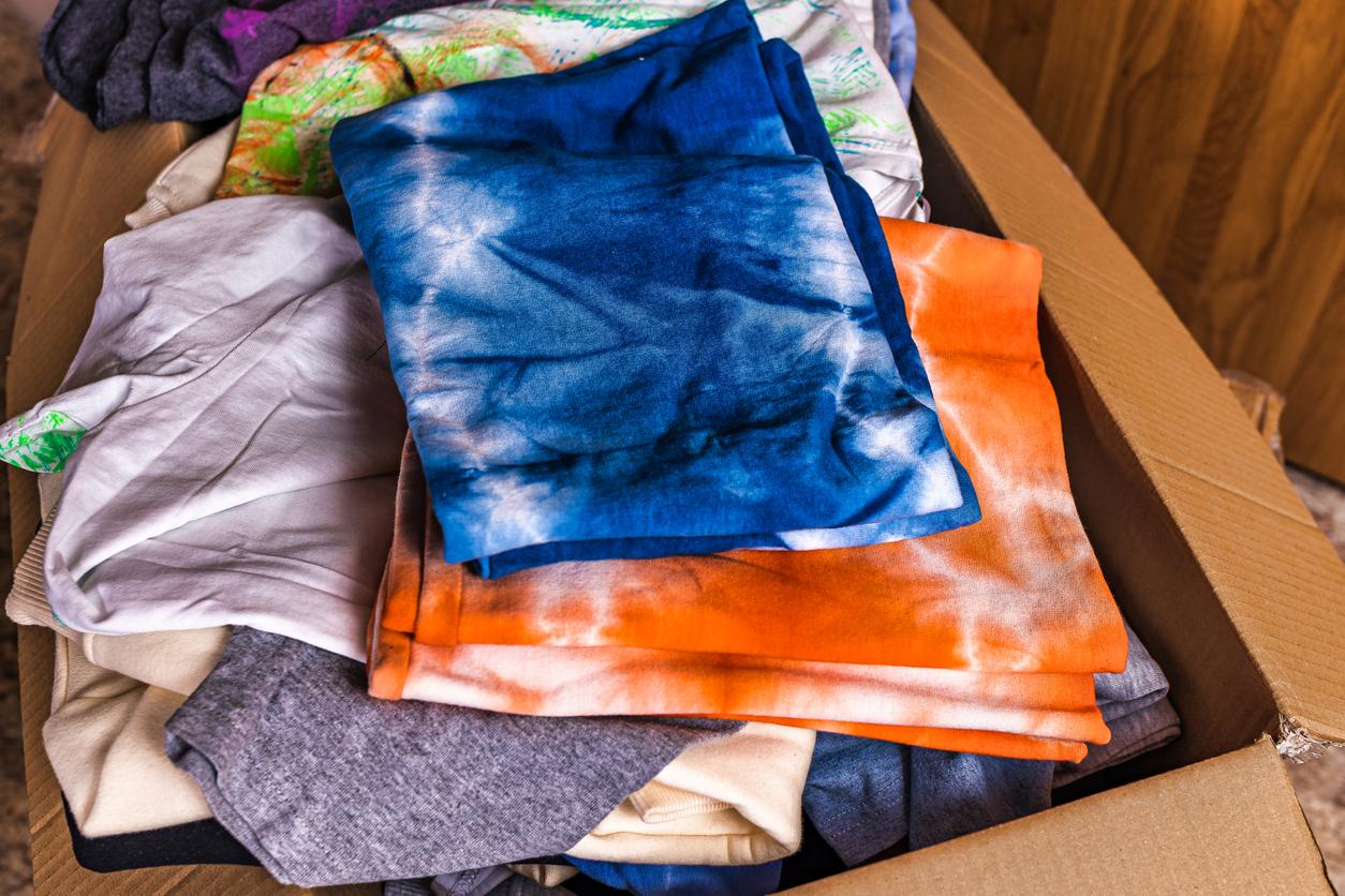 Two folded up tie-dye t-shirts on top of other clothes in a cardboard box.