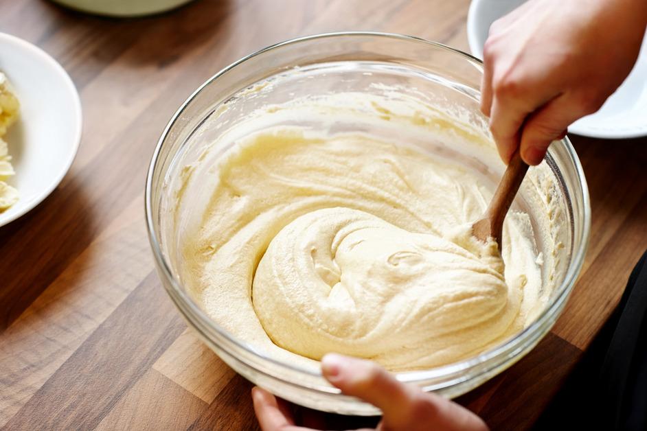 A person mixing a bowl of white batter with a wooden spoon. 