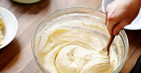 A person mixing a bowl of white batter with a wooden spoon.