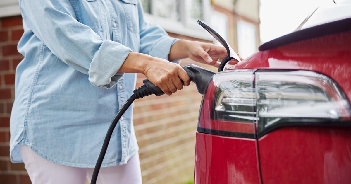 A person in a denim shirt charges their red electric vehicle. 