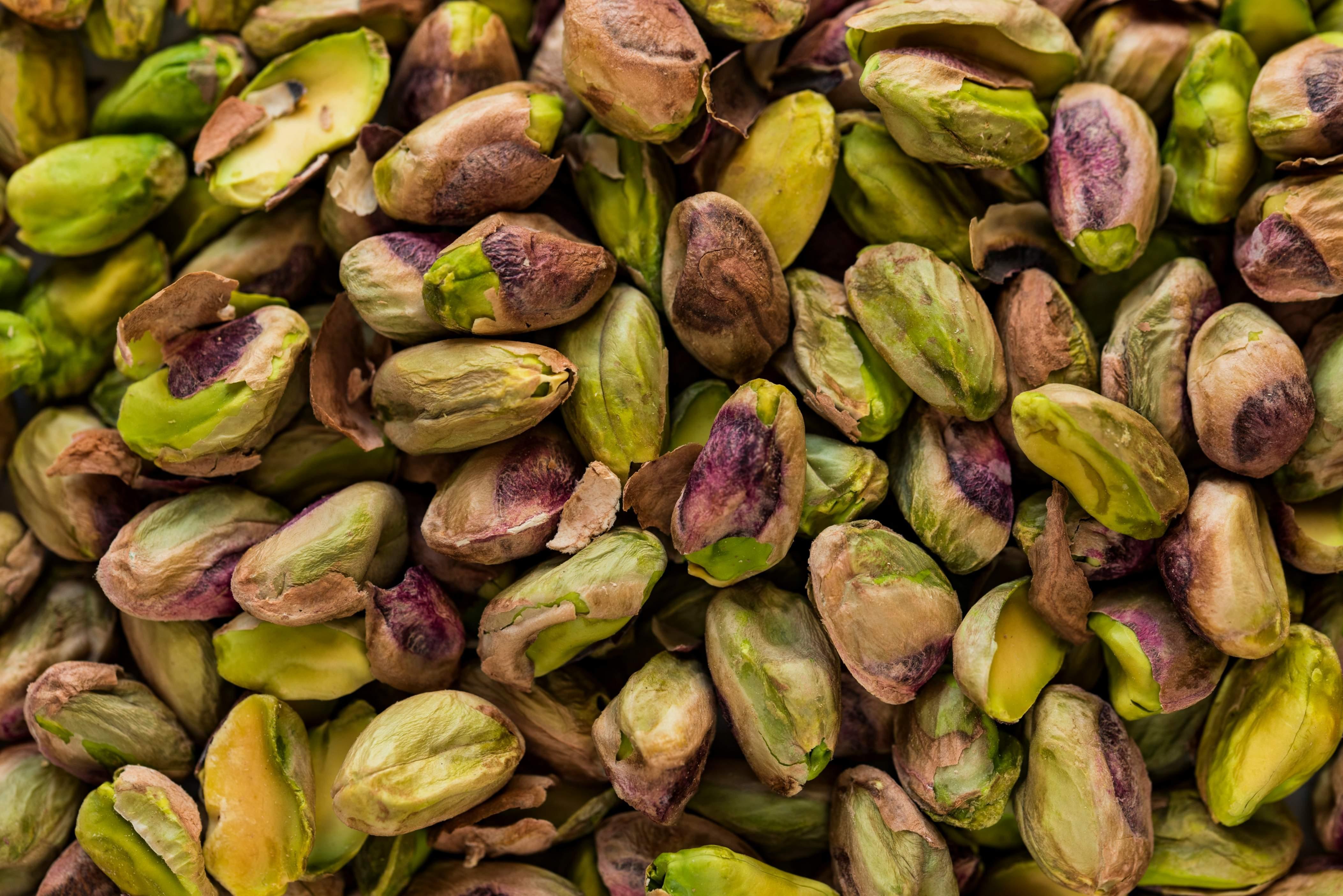 Unshelled pistachios of green and brown colors appear stacked atop one another in a large quantity.