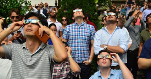 A group of people stand outside while wearing solar eclipse glasses and look up at the sky.