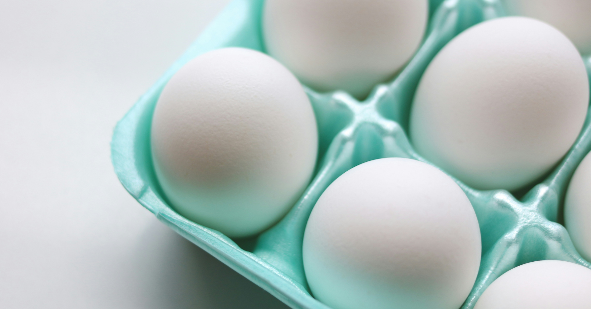 A light blue carton full of white eggs sits on a counter top.