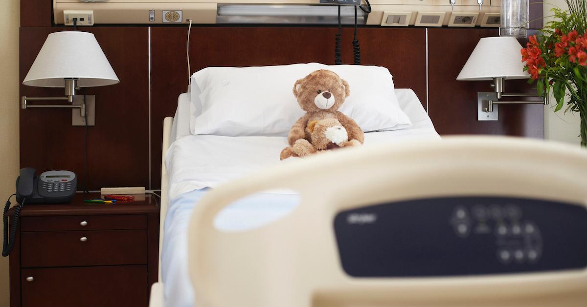 A child's hospital bed with a teddy bear on it.