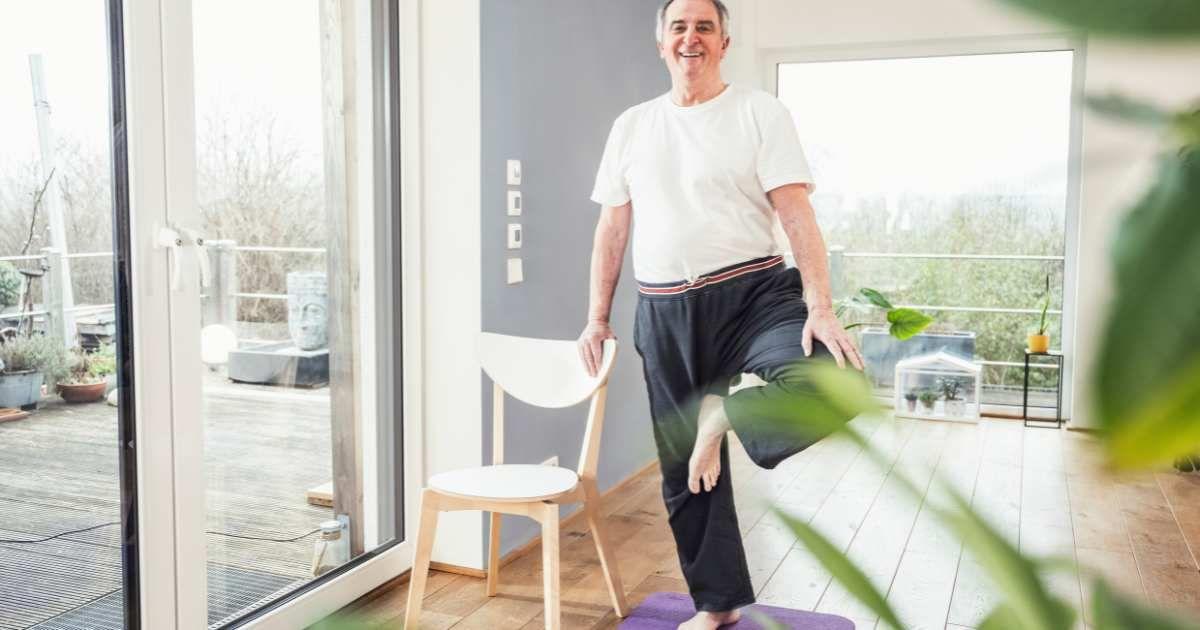 Man at home trying to balance himself on one leg while holding a chair for support. (Representative Cover Image Source: Getty Images | Westend61)