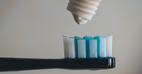 A drop of toothpaste hovers above a toothbrush