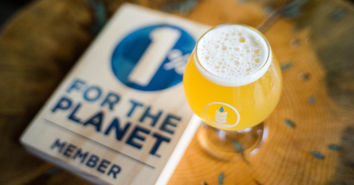 Beer in a Pure Project glass on a wooden table alongside a 1% for the Planet Member plaque.