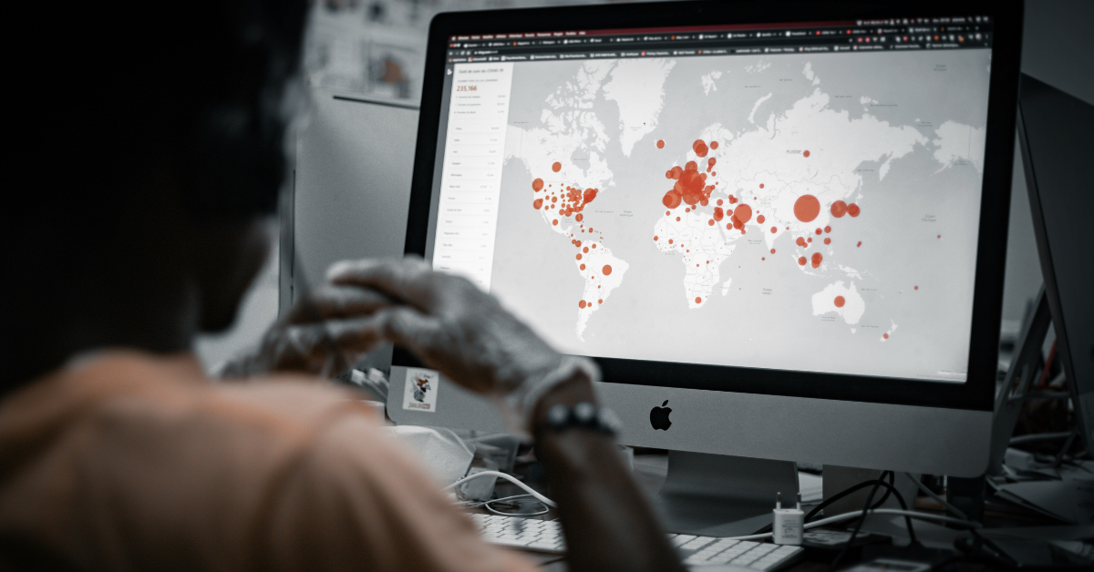 A woman looks at a simulation on her computer that features red dots across the globe