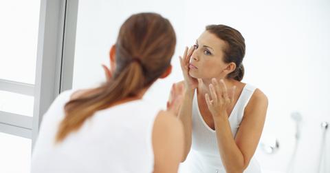 A woman wearing white looks at her face in the mirror.