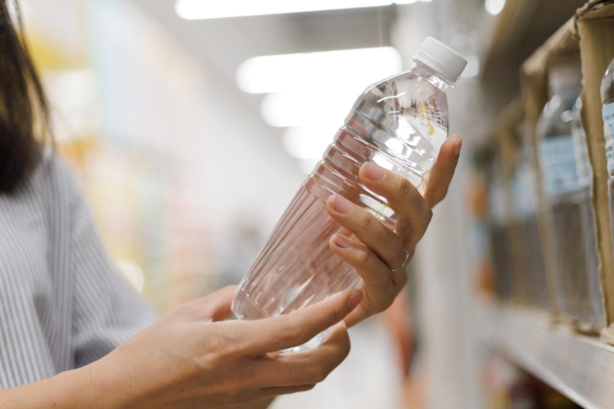 Person holding a full bottle of water near a shelf.