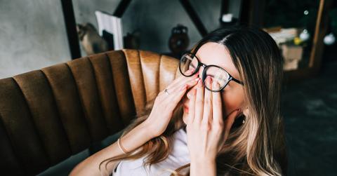 A woman rubs her eyes in pain while laying on a couch.