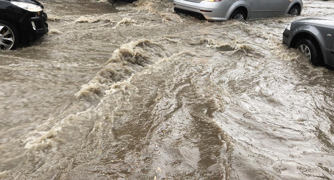 Fast-moving water on a street due to flash floods veers around three cars that are stopped in the road. 