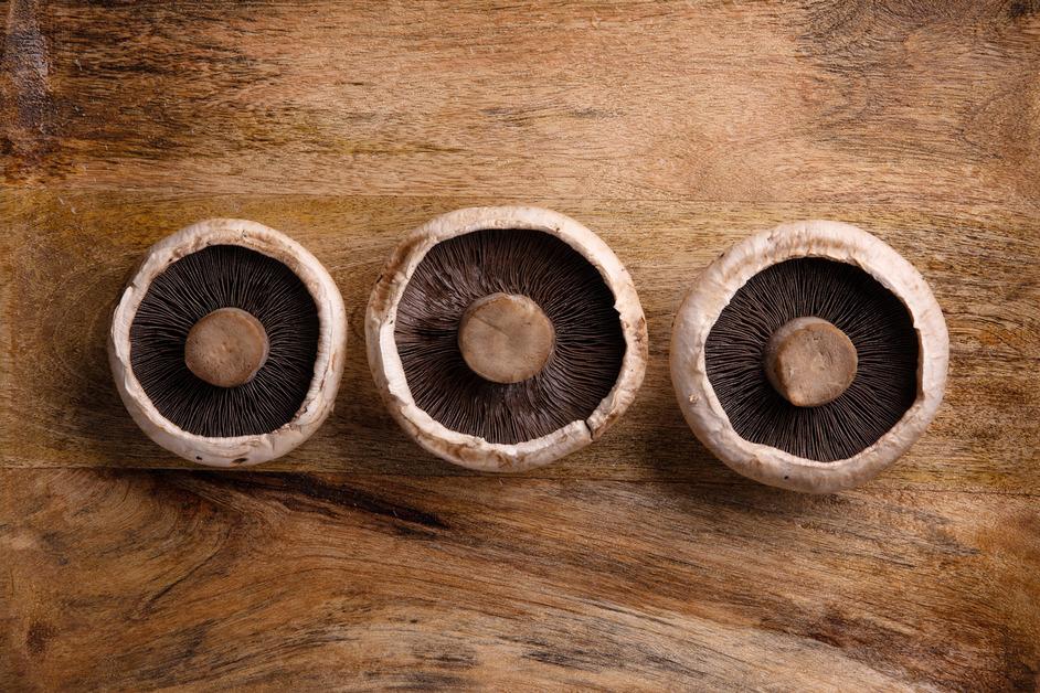 Three portobello mushrooms side-by-side on a wooden table with the gills and stems facing up. 