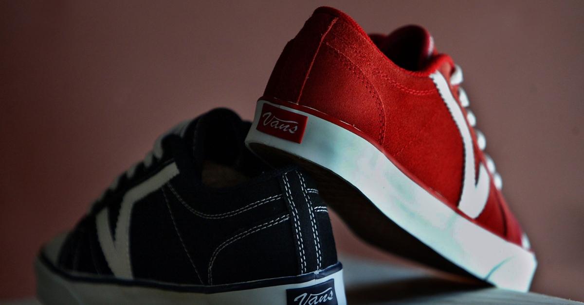 A professional photo of the back of two Vans shoes, with a black and white left shoe and a red and white right shoe. 