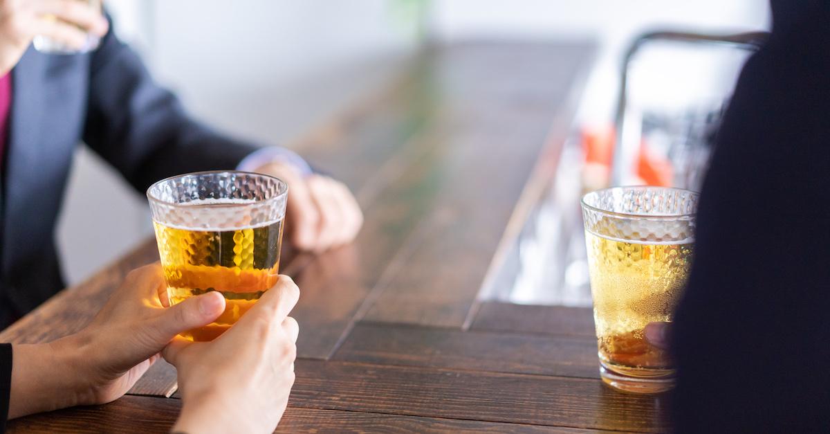 Two people sitting at a bar with beers in their hands. 