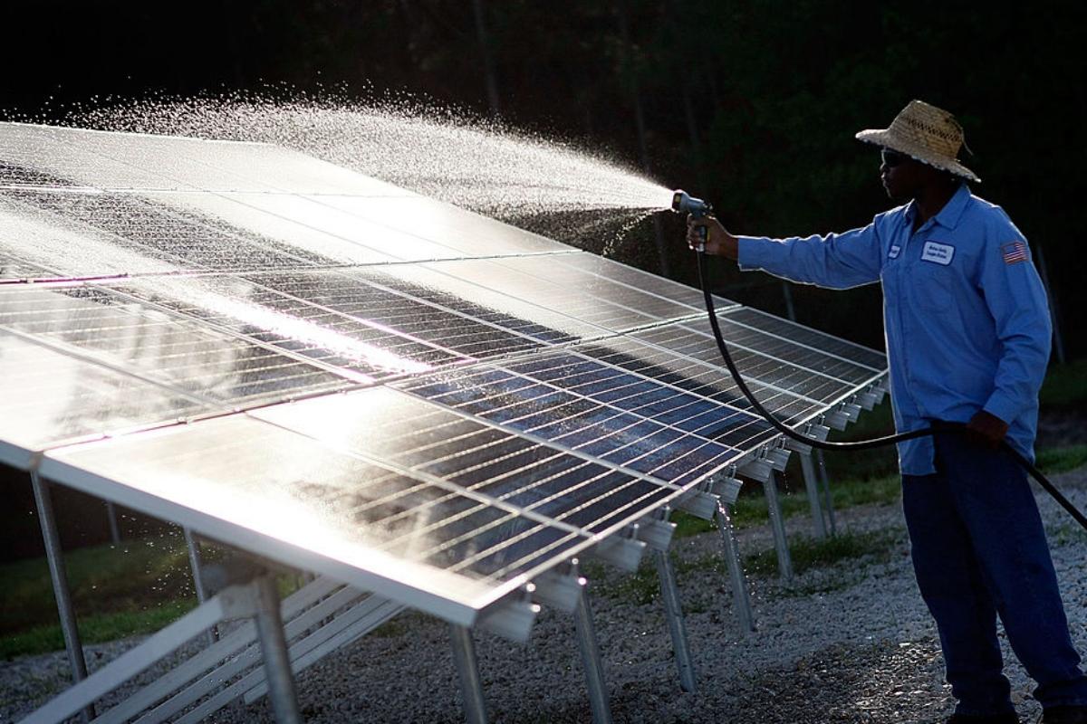 Man in straw hat sprays off solar panels