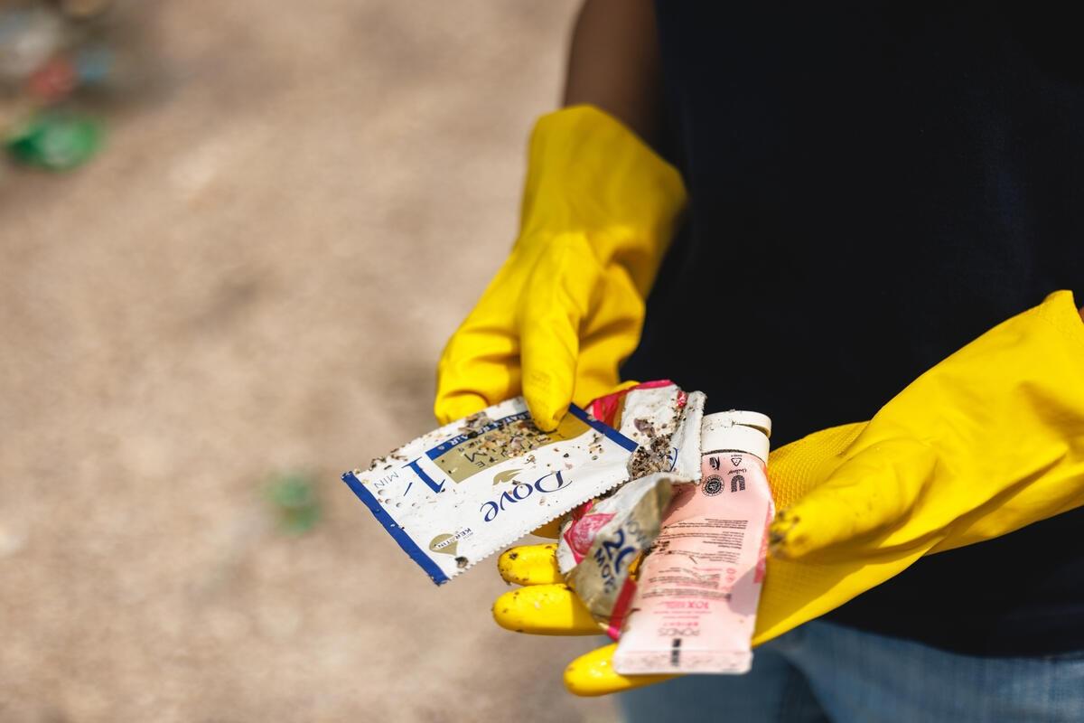 Gloved person holding plastic trash with Dove label from beach