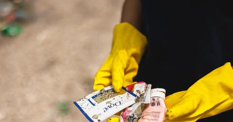 Gloved person holding plastic trash with Dove label from beach