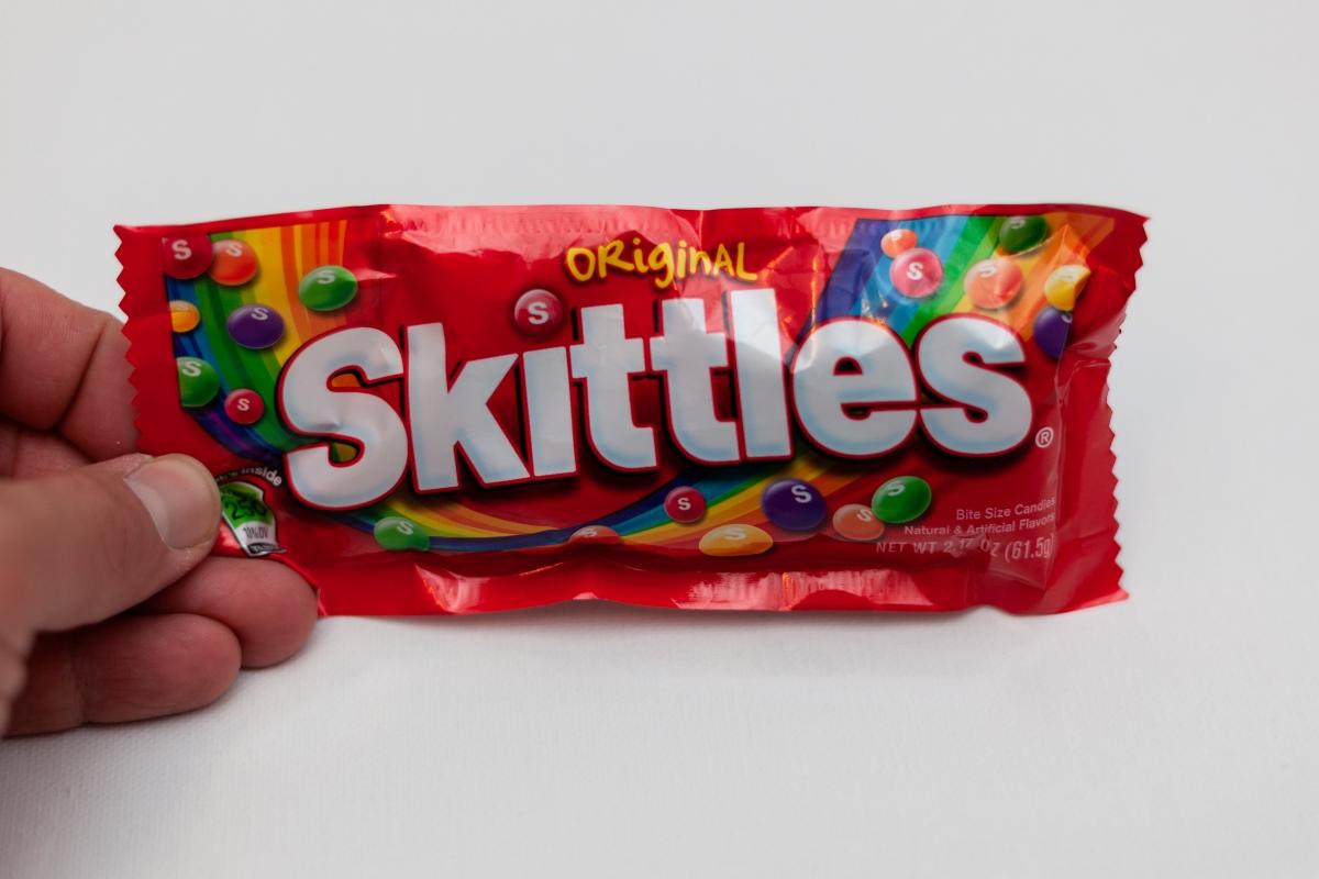 hand holding bag of Skittles on a white background