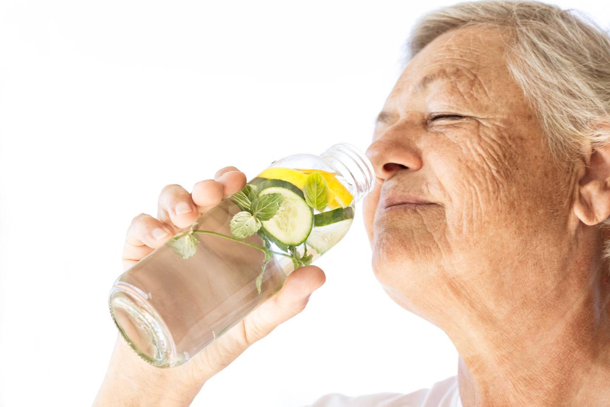 A smiling person holds a glass of water infused with lemon, cucumber, and mint.