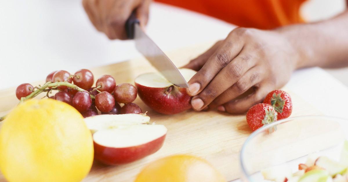 Pair of hands slices a red apple on a cutting board