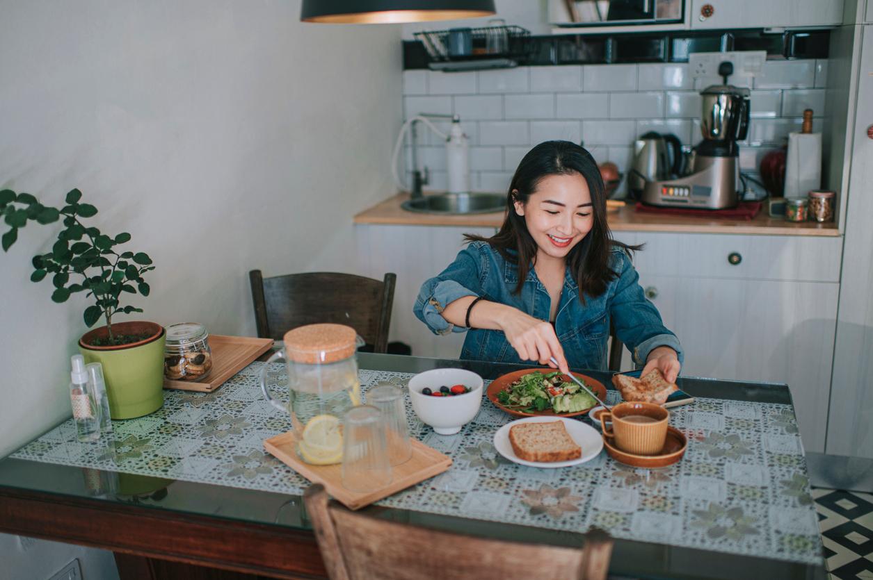 A smiling woman prepares her peanut butter toast with salad components on a separate plate and berries in a bowl beside them.