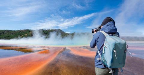 A tourist taking photos on Grand Prismatic Spring in Yellowstone National Park, Wyoming. (Representative Cover Image Source: Getty Images | Elena Pueyo)