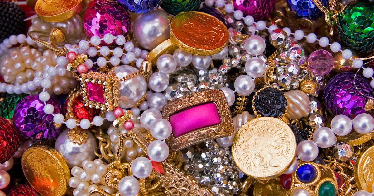 A closeup of a pile of costume jewelry, including pearl necklaces, colorful rings, and sequined baubles.