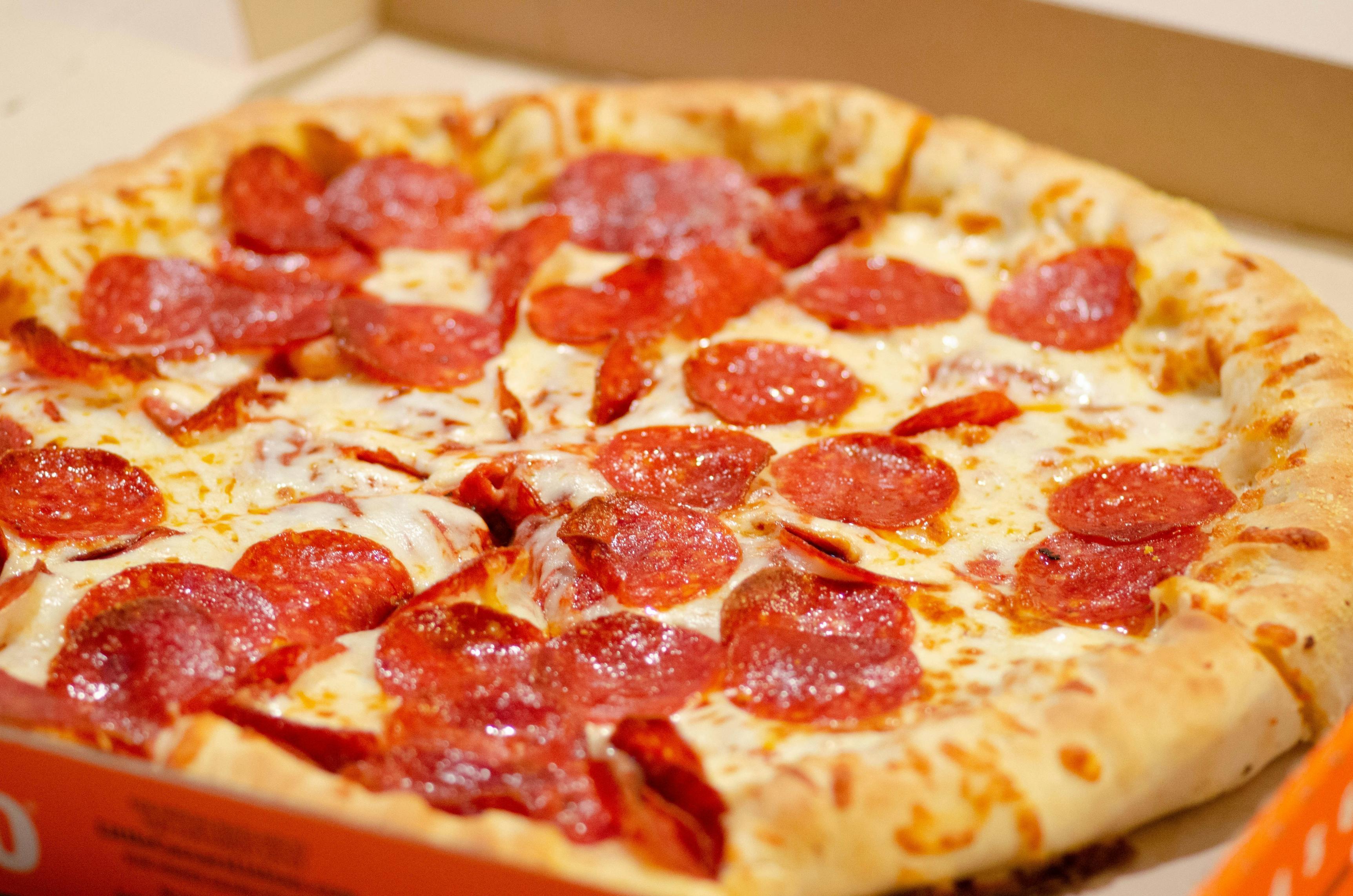 A close-up photo of a vegan pepperoni pizza in a cardboard takeout box.