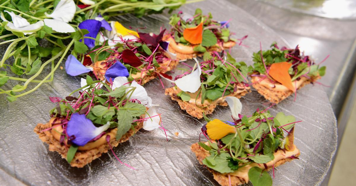 Vegan appetizers featuring edible flowers and lettuce on crackers on a gray plate