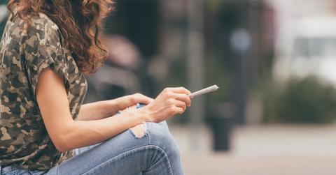 Someone sitting outside in a city with a joint.