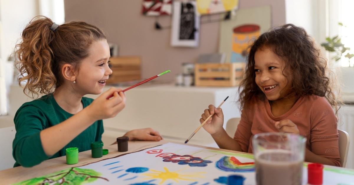 Two children holding paintbrushes work on a shared craft