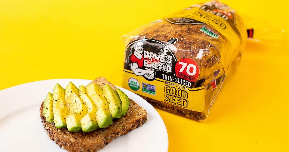 Loaf of Dave's Killer Bread Thin-Slide Organic Bread Good Seed next to a plate of avocado toast on a yellow surface