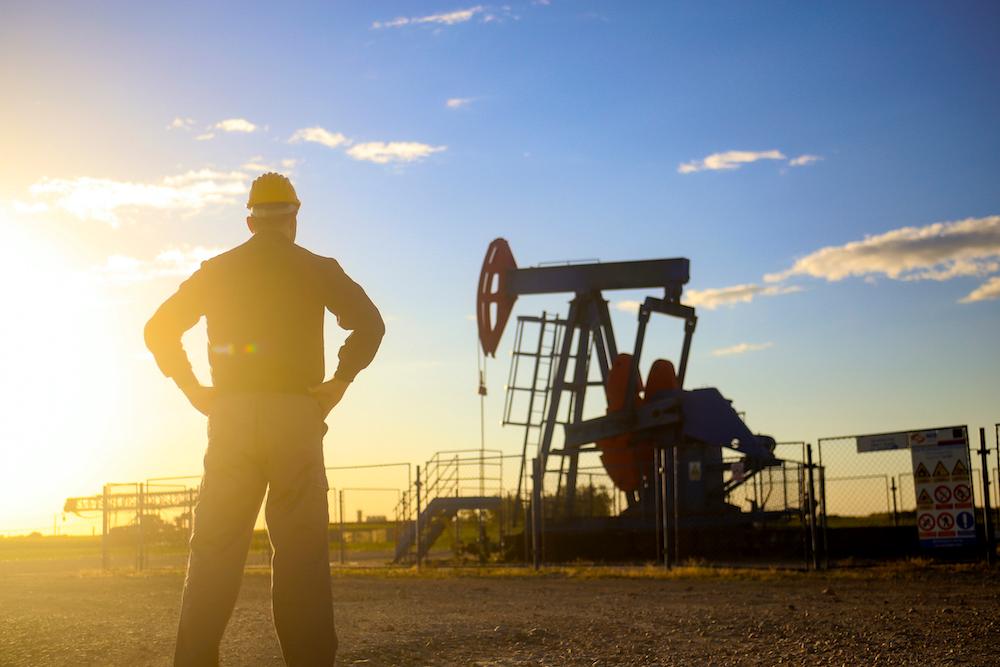 A man standing by an oil pumpjack.